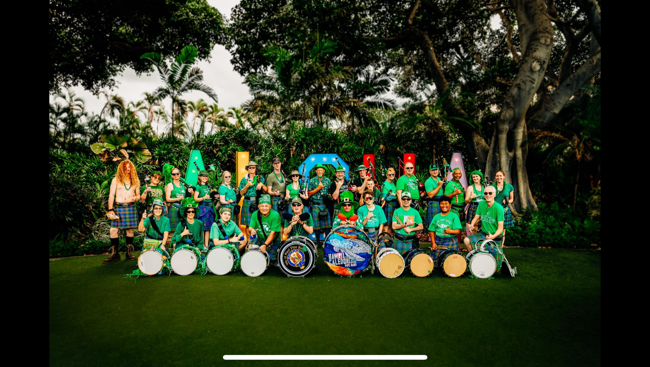 Pipers and drummers gathered in a tropical garden, pictured on the band’s fundraiser
